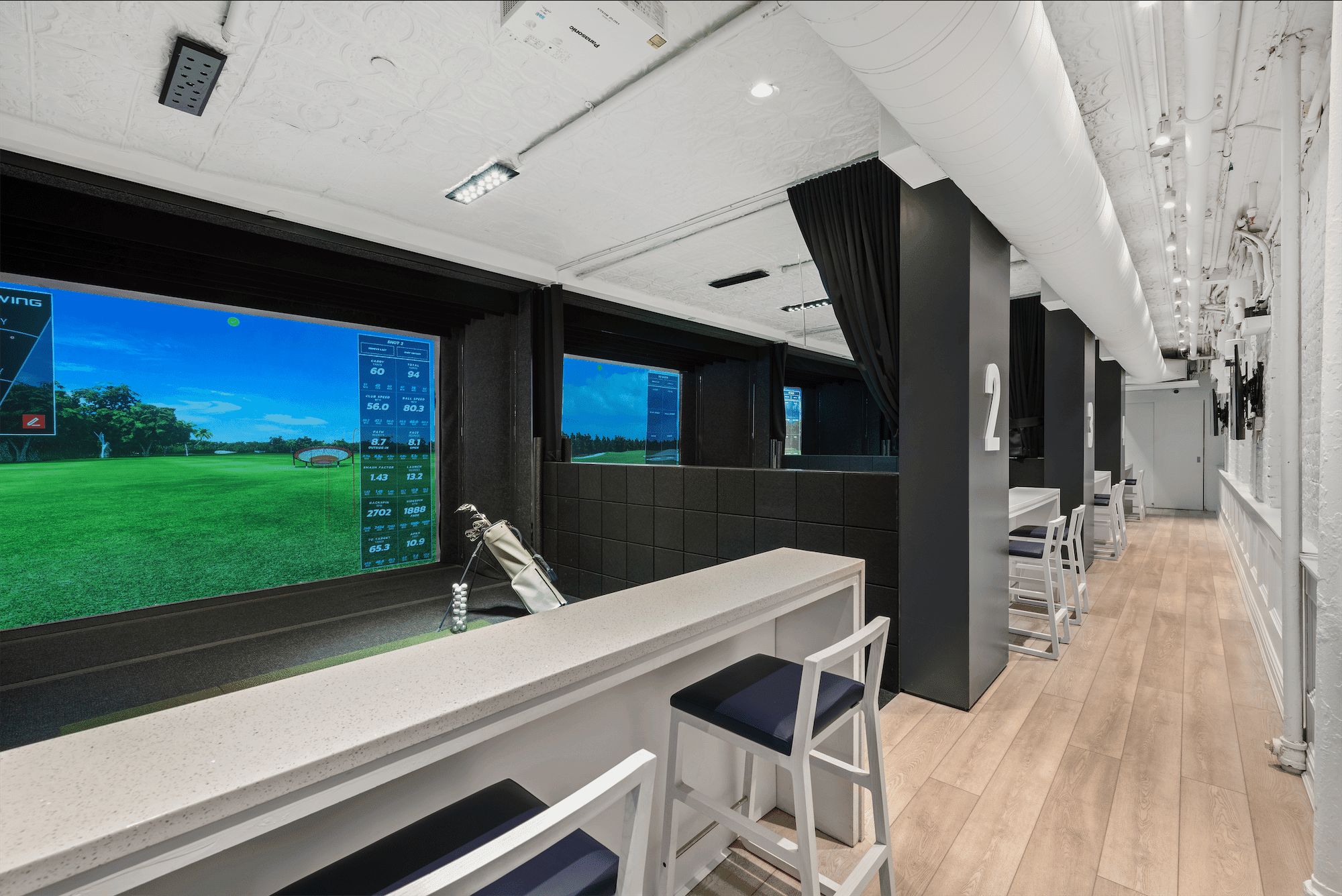 Two simulator bays side by side, each screen showing a fairway, with a long white counter and stools along the wall.