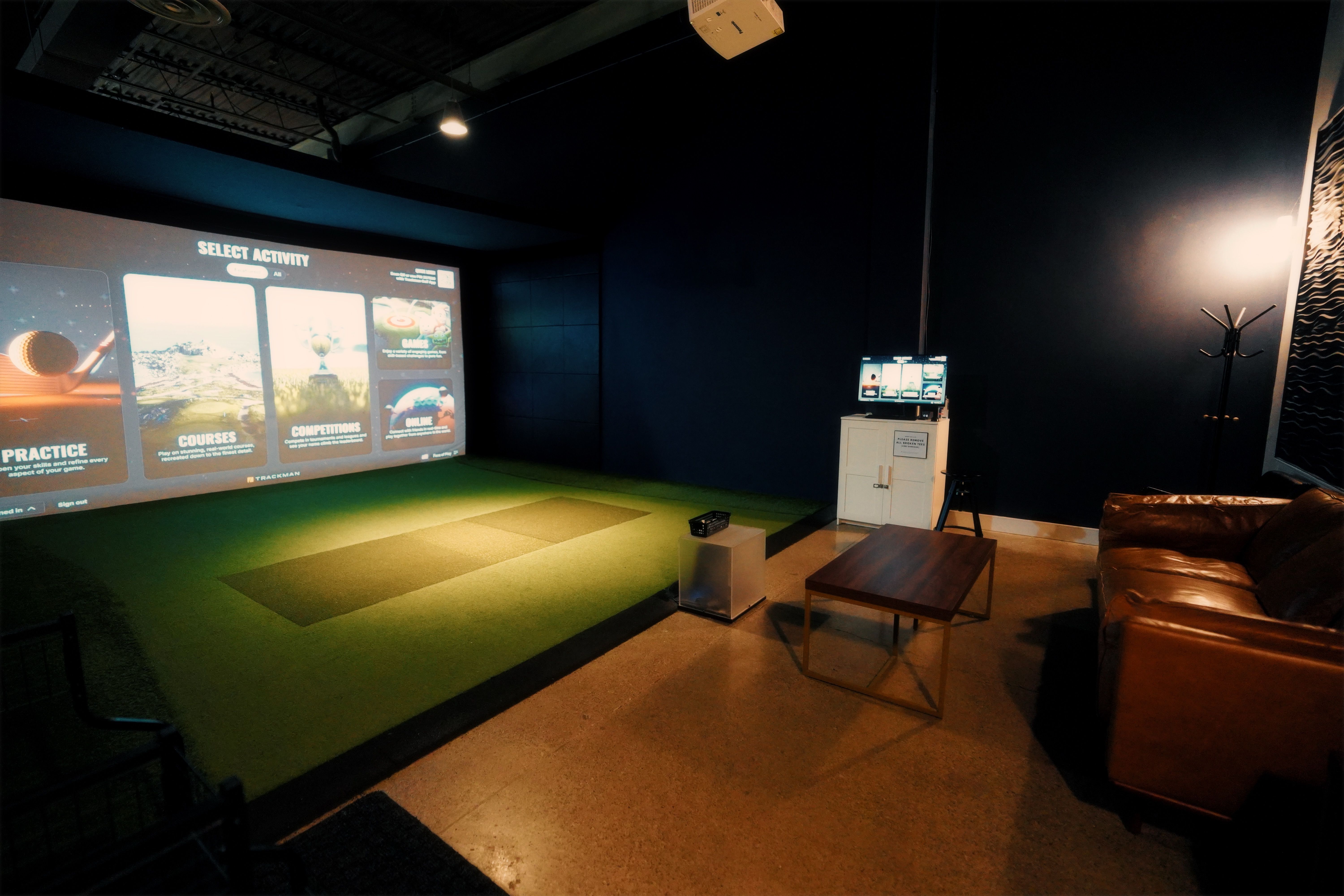 A private room with an activity-selection menu on the screen, a turf tee and a leather sofa.