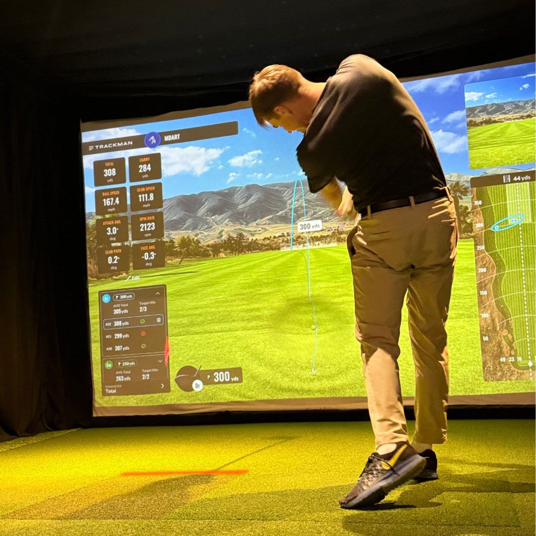 A golfer at the top of the backswing in front of a screen showing carry and ball-speed figures.