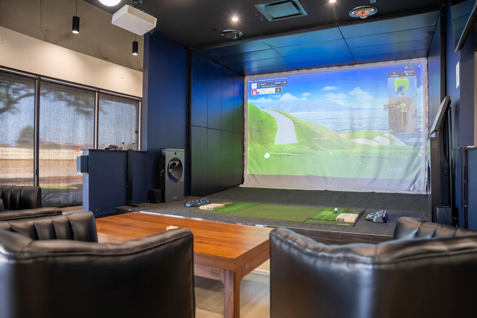 Lounge seating and a low table facing a simulator bay at 2-1-Fore Golf, Richardson, TX